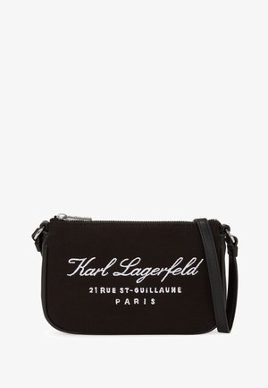 Czarna prostokątna torebka na nadgarstek z srebrnym zamkiem błyskawicznym, białym tekstem "Karl Lagerfeld 21 Rue St-Guillaume Paris" i czarnym odpinanym paskiem.