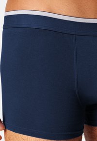 Boxers bleu marine en tissu lisse, avec une ceinture contrastante gris clair. La vue en gros plan met en valeur la texture du textile.
