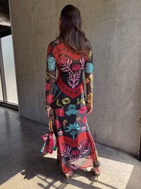 Lang, gjennomsiktig kjole med flerfargede blomster- og hjerte-mønstre på svart bakgrunn. Kombinert med en mønstret håndveske og høye hæler.