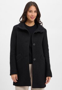 Black wool blend coat with a button closure, wide collar, and two front pockets. Smooth texture and tailored fit. Subtle design details.