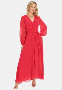 Długa różowa sukienka z szyfonu z długimi rękawami, falbaniastym dekoltem w kształcie litery V, paskiem w talii i lekko opadającą spódnicą z asymetrycznym dołem.