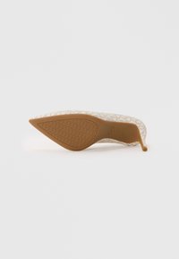 Scarpa con tacco alto beige con tomaia in tessuto fantasia e punta appuntita. Suola in gomma color cuoio con grip strutturato. Design del tacco sottile ed elegante.