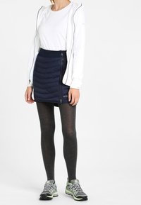 Vit långärmad skjorta, marinblå puffkjol med sidodragkedja, grå leggings och grå skor med gröna detaljer. Enkelt och funktionellt utomhuskl äder.