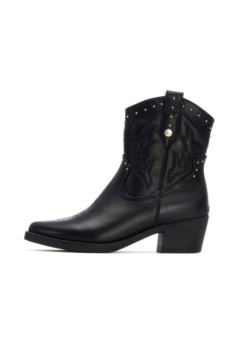 Bota vaquera de cuero negro con bordado estilizado, tachuelas doradas en la parte superior, punta afilada y tacón apilado.