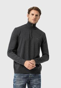 Dunkelgrauer Zip-Kragen-Pullover mit geripptem Kragen und Bündchen, aus einem strukturierten Strickstoff, kombiniert mit hellblauen, lässig ausgefransten Jeans.