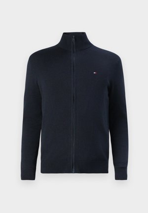 Námornícky zipsový sveter s vysokým golierom, ribbovanými manžetami a spodným lemom, s malou logom akcentom na ľavej hrudi. Hladká pletená textúra.