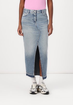 Light blue denim maxi skirt with a front slit and raw hem. Features a five-pocket design and belt loops. Paired with silver sneakers.
