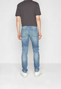 Dopasowana szara koszulka z podwiniętymi rękawami w połączeniu z jasnoniebieskimi rurkami. Białe sneakersy dopełniają zestaw. Minimalistyczny design, gładkie materiały.