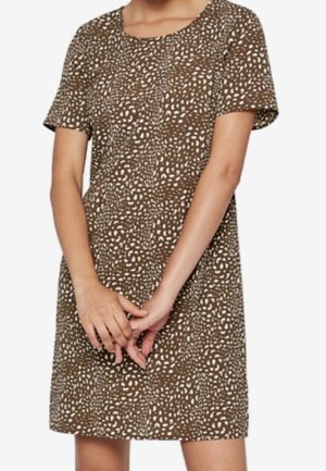 Woman wearing a short-sleeve, knee-length brown dress with a white abstract dotted pattern, standing with hands clasped in front.