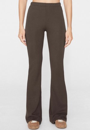 Bruine geribbelde wijde broek met voorste splitjes gedragen door een persoon die staat met ontspannen handen langs de zij.
