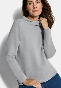 Grijze textuur lange mouwen top met een hoge kraag en ribbelpatroon. Draagt comfortabel met blauwe denim, met een relaxte pasvorm en zachte stof.
