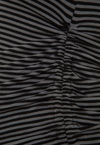 Czarna i szara tkanina w paski z marszczoną teksturą, z szeregiem pionowych fałd tworzących efekt falowania na całej powierzchni.