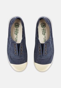 Tengerészeti pamut slip-on cipők arany szemekkel és krémszínű gumi orrkupakkal. A talpbetét zöld logót tartalmaz, amely az öko-barát anyagokat jelzi.