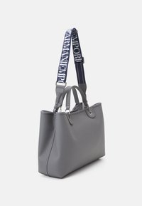 Szara skórzana torba typu tote z dwoma uchwytami i odpinanym granatowym paskiem z białymi akcentami logo. Gładka faktura i usztywniony kształt.
