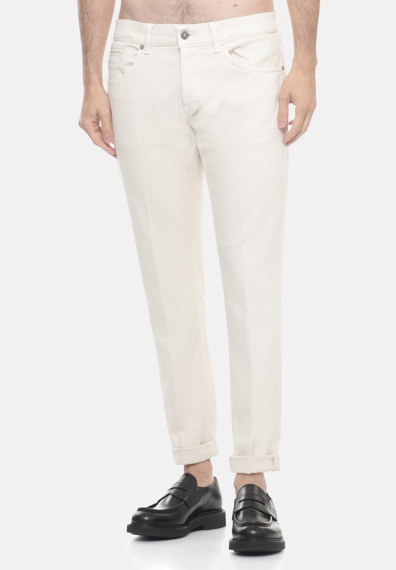 Pantaloni in cotone beige con design a gamba dritta, orli risvoltabili, tasche laterali e chiusura frontale con bottone, abbinati a scarpe nere senza lacci.