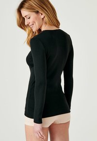 Top nero a maniche lunghe con un motivo testurizzato e scollatura rotonda, caratterizzato da un design aderente e un orlo posteriore leggermente allungato.