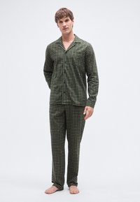 Conjunto de pijama a cuadros verdes y negros que incluye una camisa abotonada con cuello y pantalones a juego, confeccionados con una tela suave.