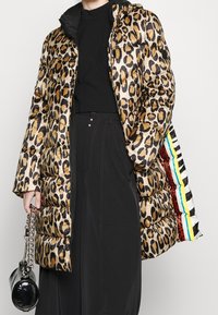 Abrigo tipo puffer con estampado de leopardo y textura brillante, silueta oversized y capucha negra. Presenta acentos de rayas multicolores en el interior.