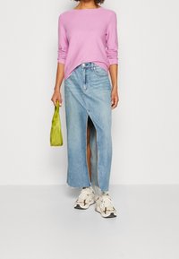 Pull en laine rose à manches longues, jupe maxi en denim bleu clair avec fente avant, baskets blanches et un petit sac vert. Combinaison d outfit décontracté.