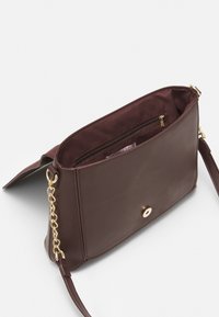 Hnědá kožená kabelka s řetízkem a popruhem, vybavená magnetickým zapínáním a vnitřní kapsou na zip. Hladká textura bez výrazných vzorů.