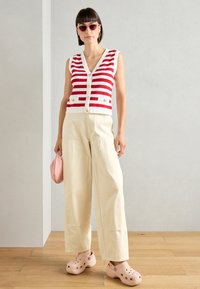 Red and white striped sleeveless sweater, beige wide-leg pants, pink handbag, and light pink clogs. Minimalist design with buttons and pockets.