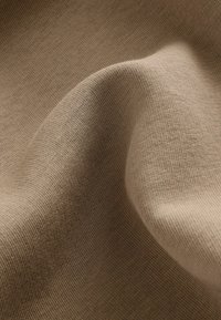 Beige knit fabric with a smooth texture, displayed in gentle folds revealing a fine, even weave and soft surface detail.