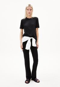 Zwarte t-shirt met korte mouwen, wit shirt geknoopt om de taille, zwarte broek en paarse instappers. Eenvoudig, casual ontwerp zonder patronen.