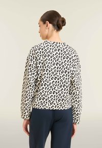Felpa con stampa leopardata in crema con macchie nere; presenta maniche lunghe e scollatura arrotondata; abbinata a pantaloni blu navy, vista da dietro.