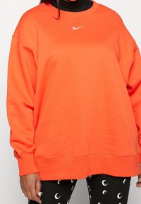 Orange Nike sweatshirt med rund halsringning och sänkta axlar. Har en liten vit logotyp på bröstet och ribbade ärmslut.