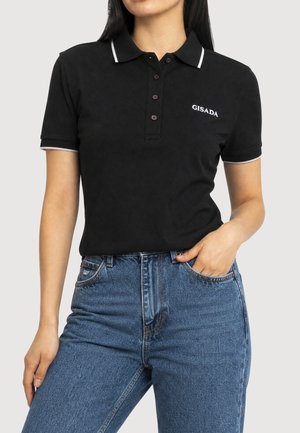 Femme portant un polo noir à manches courtes avec bord blanc et logo "GISADA", associé à un jean bleu taille haute.