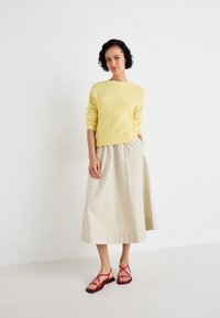 Yellow wool sweater, beige midi skirt, and red strappy sandals with a low heel. Light texture, simple design, and soft colors.
