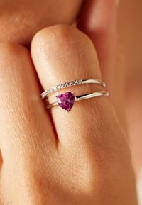 Two silver rings on a finger, one with a row of small diamonds, the other with a heart-shaped purple gemstone.