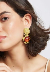 Goldene Ohrringe mit einem strukturierten, runden Oberteil und einem größeren bernsteinfarbenen Stein darunter, verziert mit filigranen Details, die kontrastierende Materialien zur Schau stellen.