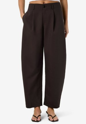 Kõrge vöökohaga laiade jalgadega mustad püksid esikortsude, küljetaskute ja nööpidega, kantud mustade avatud varbaga sandaalidega.