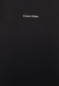 Černé bavlněné tričko s kulatým výstřihem a bílým logem "Calvin Klein" uprostřed na hrudi. Hladká textura, minimalistický design.