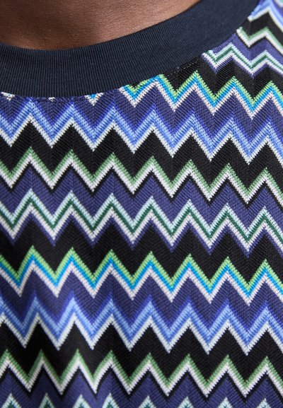 Lühikeste varrukatega särk, millel on sinise, rohelise, musta ja valgega siksakiline muster. Materjal on kudum, millel on ühtlane tumesinine soonikkoes krae.