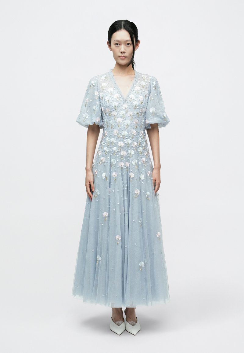 Ljusblå tyllklänning med V-ringning och puffärmar, prydd med blommig brodyr och pärlbroderi. Kombinerad med vita spetsiga högklackade skor.