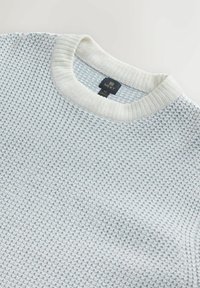 Pulover albastru deschis cu un model texturat și guler alb cu bătăi. Prezintă un etichetă cu denumirea "NEXT." Material moale, tricotat.