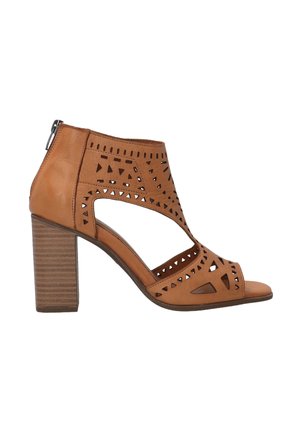 Brune læder hælede sandaler med udskårne geometriske designs, en lukket ryg og en tekstureret blokhæl. Åben tå med lynlås lukning.