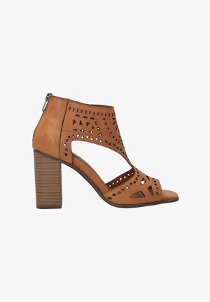 Brown leather heeled sandals featuring cut-out geometric designs, a closed back, and a textured block heel. Open toe with a zipper closure.