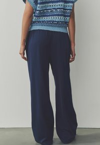 Pantaloni largi bleumarin cu un design texturat din dungi. Purtați cu un top tricotat scurt cu mâneci, cu un model albastru, evidențiind o vedere din spate relaxată.