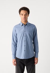 Light blue button-up shirt with a pointed collar, long sleeves, and a slim fit. Features a subtle logo and dark buttons.