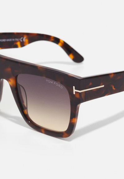 Ochelari de soare din birmă cu un cadru dreptunghiular gros, lentile cu gradient, accent argintiu cu marca "Tom Ford" pe bratul ochelarilor.