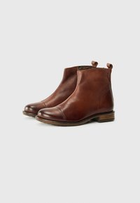 Bottines en cuir brun avec un bout arrondi, un cap décoratif et deux languettes. Elles disposent d'un talon en bois empilé et d'une texture lisse.