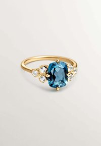Anillo de oro con una gran piedra azul, flanqueada por tres piedras claras y redondas a cada lado, con una banda lisa.