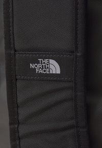 Zwarte stofpatch met het "THE NORTH FACE" logo in het wit. Het oppervlak heeft een gestructureerde weving en geborduurde randen voor duurzaamheid.