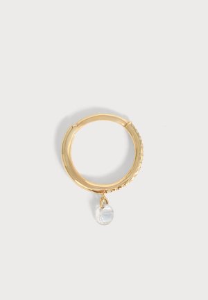 Boucle d’oreille créole en or avec un petit pendentif cristal transparent suspendu en bas, sur un fond clair uni.
