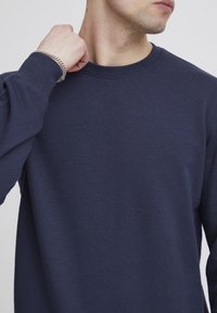 Tengerészkék, hosszú ujjú póló puha pamutból, kerek nyakkal és egyszerű kialakítással, varrási részletekkel az illesztéseken.