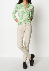 Grön blommönstrad skjorta med knappar och trekvartsärmar, matchad med beige byxor och svarta slip-on skor med tjocka sulor.