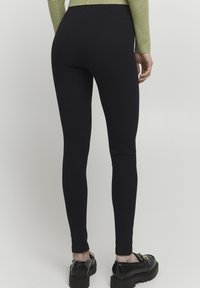 Fekete bordázott leggings, rugalmas derékkal, testhez simuló fazon, teljes hosszúságú borítással, fekete vastag talpú cipőkkel kombinálva.